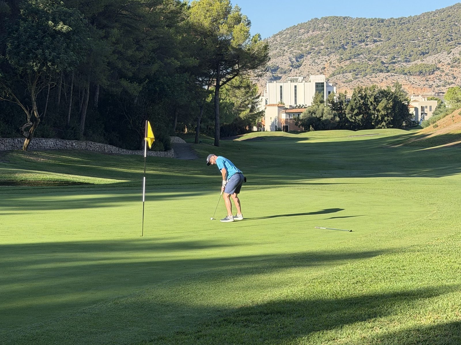 Christopher putting on a sunny golf green, hills in the background