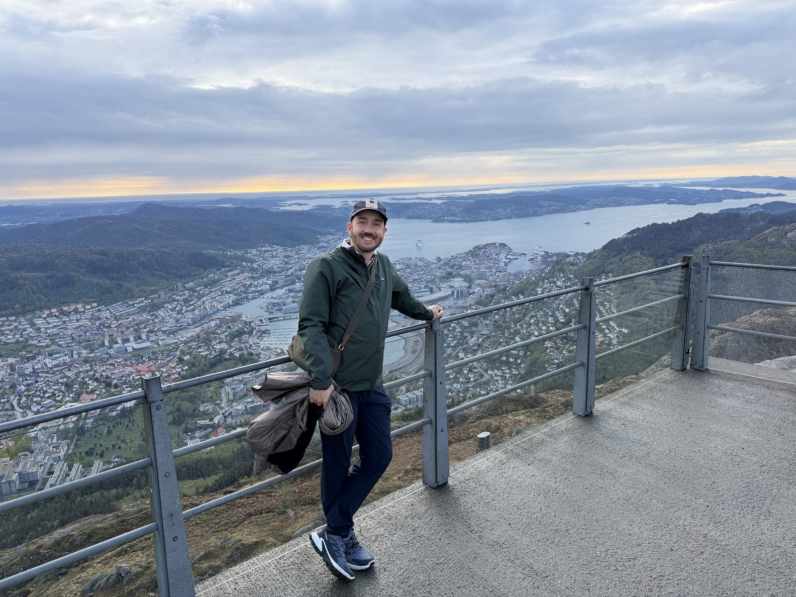 Christopher smiling at a viewpoint high above Bergen, Norway, with the fjord behind him